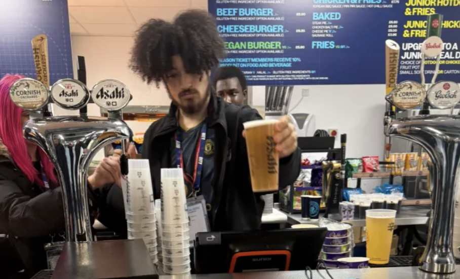 Một nhân viên mặc áo Manchester United đang rót bia phía sau quầy bar tại Etihad trong trận derby Mot nhan vien mac ao Manchester United dang rot bia phia sau quay bar tai Etihad trong tran derby